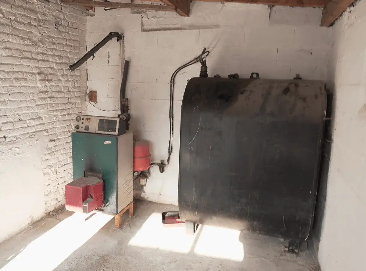Chaudière et grande cuve noire pour le chauffage fioul, installées dans une pièce aux murs de briques blanches.