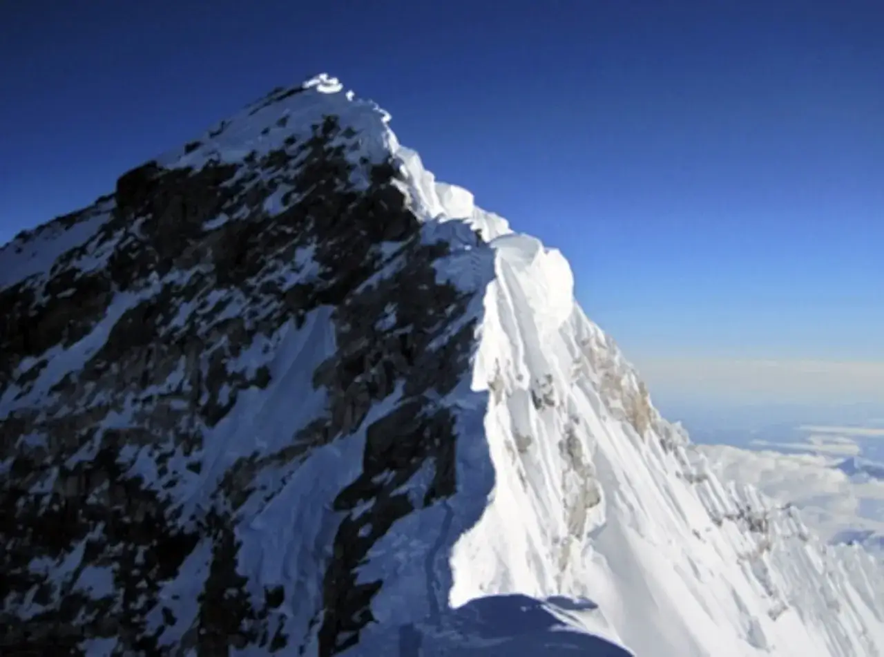Szczyt Mount Everest, którego wysokość zapiera dech w piersiach, pokryty śniegiem i lodem, lśni w słońcu pod błękitnym niebem.
