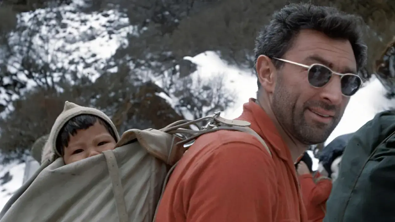 Guido Magnone, lunettes de soleil, porte un bébé dans un sac à dos sur un sentier enneigé.