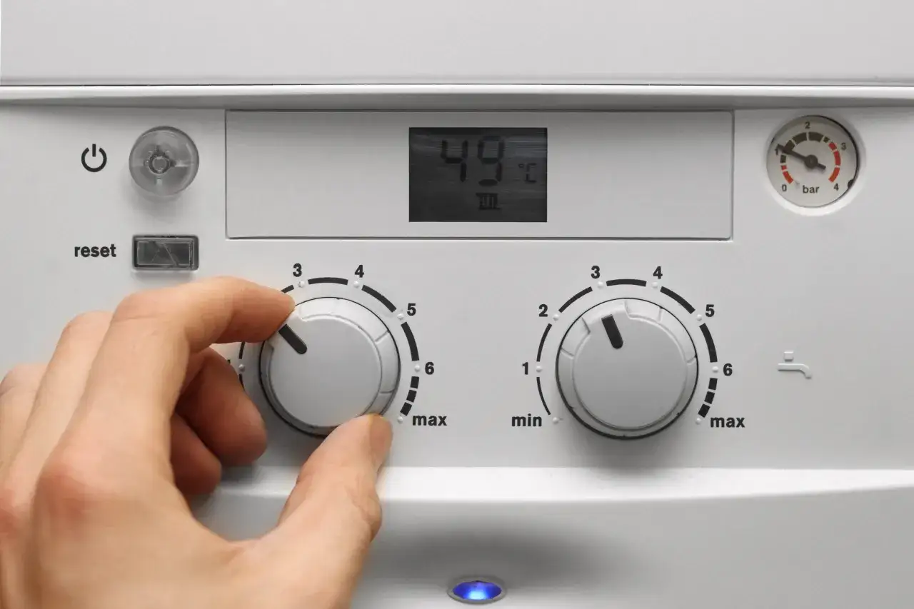 Mano che regola la manopola di una caldaia, con display a 49°C. La caldaia non parte per i termosifoni, forse un problema di impostazione.