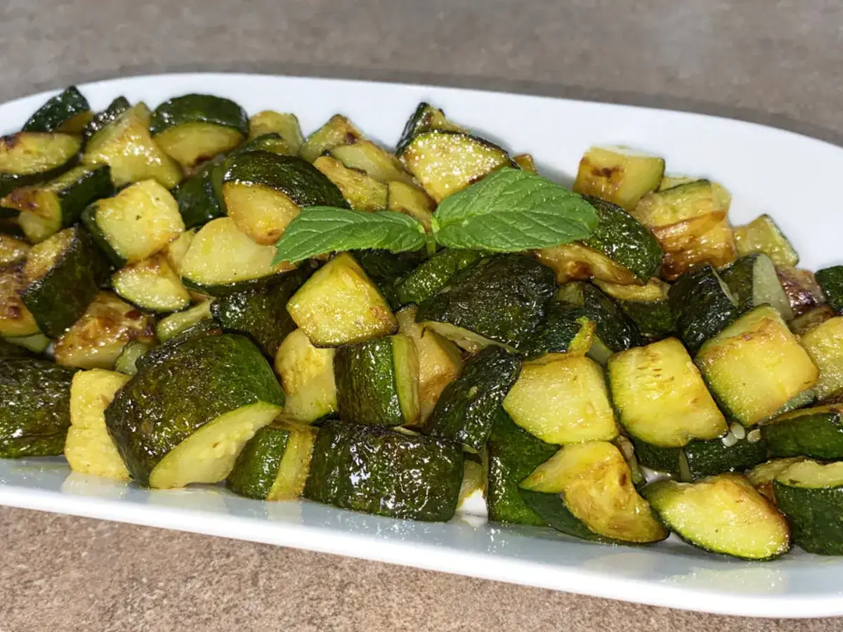 Zucchine in padella, tagliate a pezzi e dorate, guarnite con foglie di menta fresca. Un contorno semplice e gustoso.