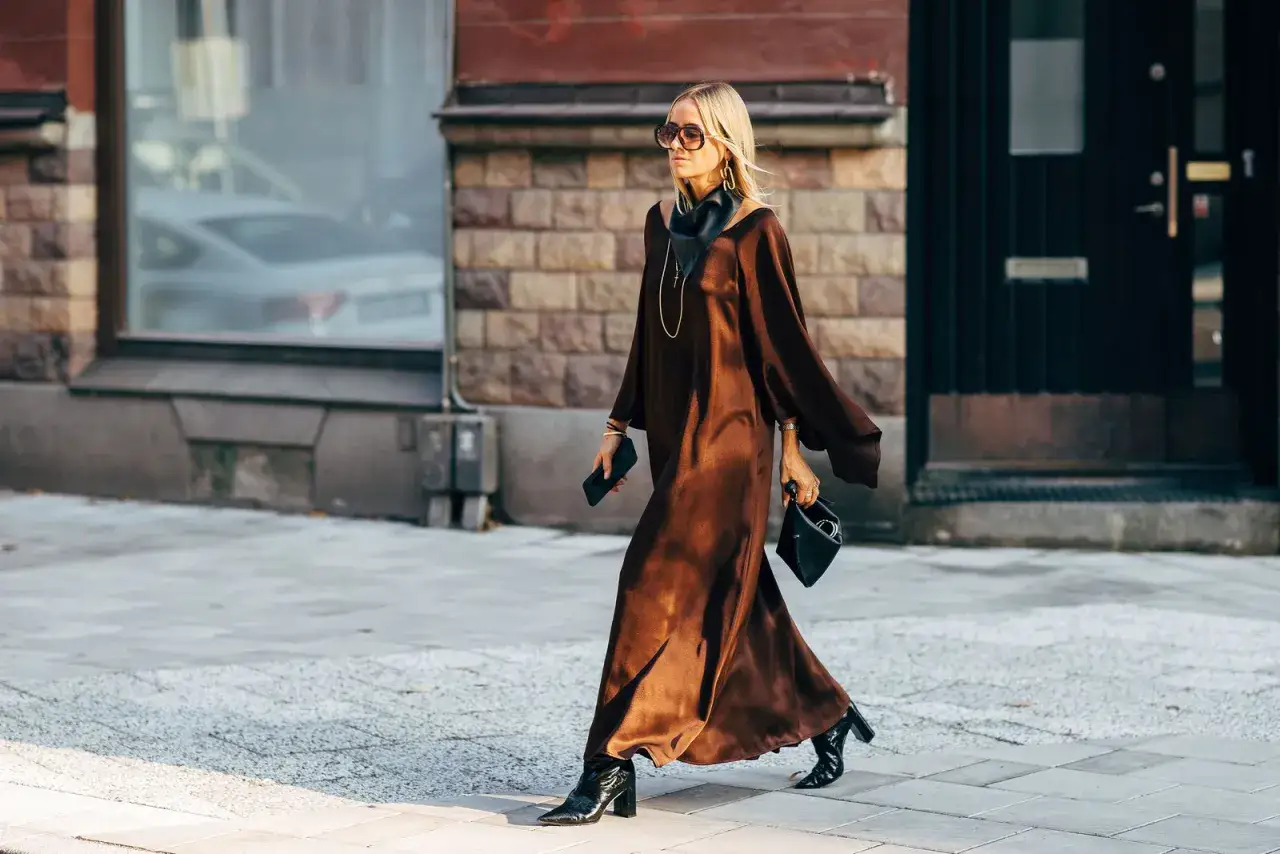 Marie Serneholt i en elegant brun klänning och svarta stövlar, på väg längs en stadsgata.