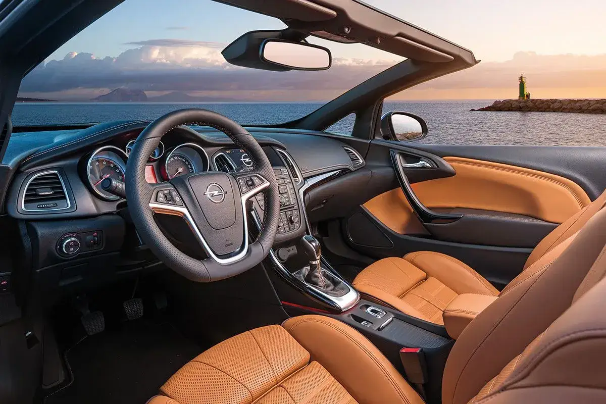 Wnętrze kabrioletu Opel Cascada z brązową skórzaną tapicerką, kierownicą i widokiem na morze.