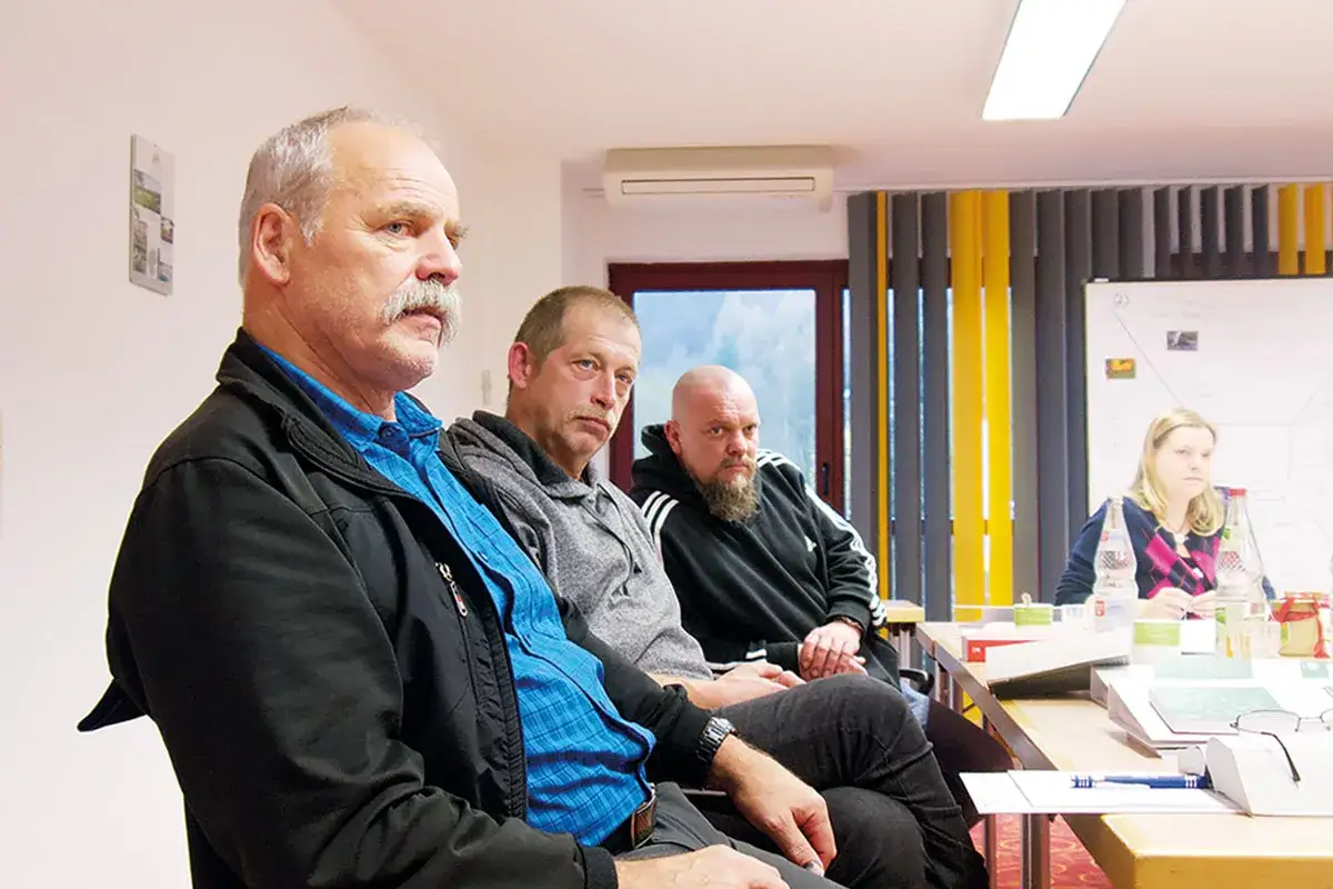 Männer und eine Frau sitzen an einem Tisch, diskutieren die Voraussetzungen für Kurzarbeit.