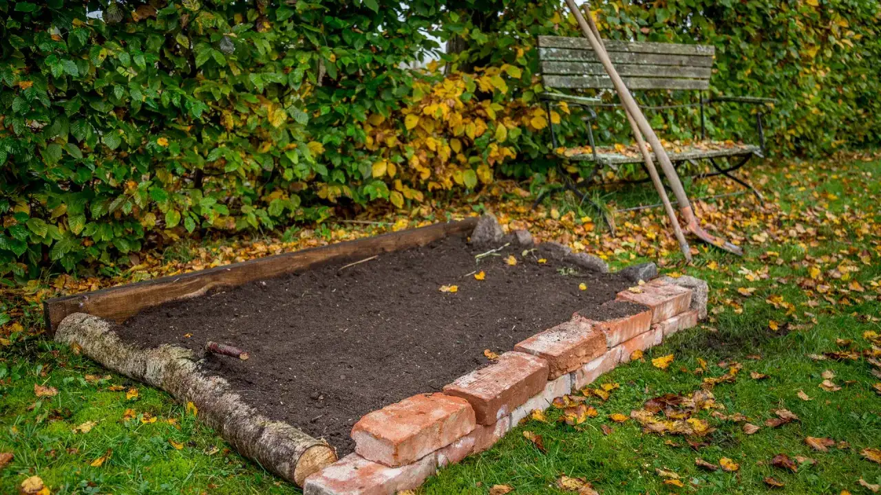 Ein neues Beet anlegen: Erde ist aufgeschüttet, umrandet von Holz und Ziegeln. Gartengeräte und eine Bank stehen bereit.
