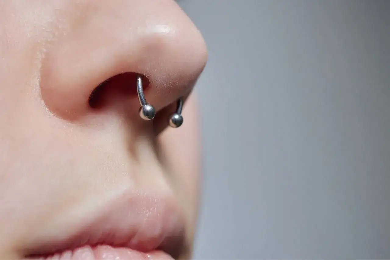 Metalowy kolczyk w kształcie podkowy zdobi nos, podkreślając styl osoby. Ile goi się septum? To zależy od indywidualnego procesu.