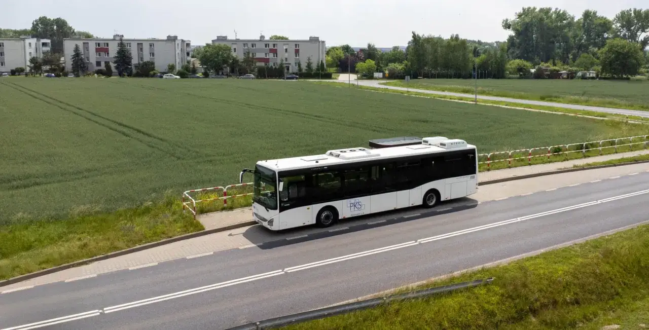 Autobus PKS jedzie drogą obok pola. Chcesz wiedzieć, jak dojechać do Jarosławca autobusem? Ten widok może być częścią Twojej podróży.