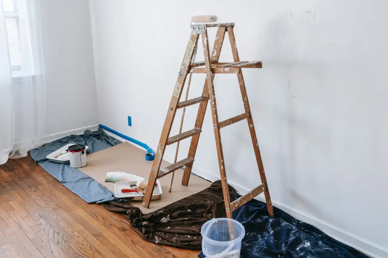 Pr&eacute;paration pour une nouvelle peinture : &eacute;chelle en bois, pots de peinture, rouleaux et bacs sur des b&acirc;ches bleues et marron.