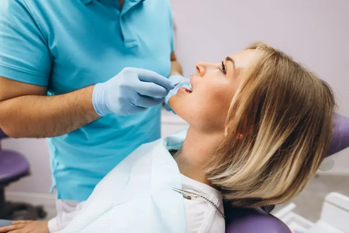 Dentysta bada jamę ustną pacjentki, sprawdzając ewentualne powikłania po usunięciu kamienia nazębnego.