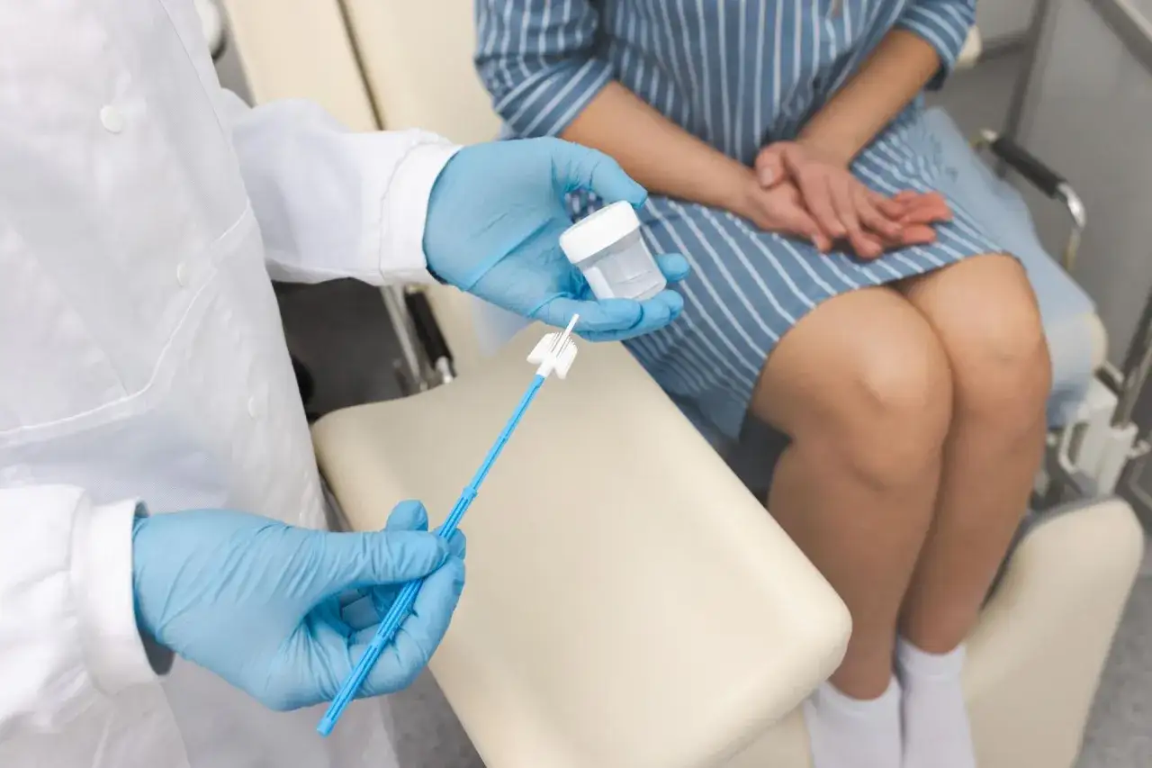 Lekarz w rękawiczkach pokazuje pacjentce pojemnik i szczoteczkę do pobrania wymazu. Może to być związane z badaniem cytologiczny lub leczeniem, np. przy użyciu **Primolut Nor**.