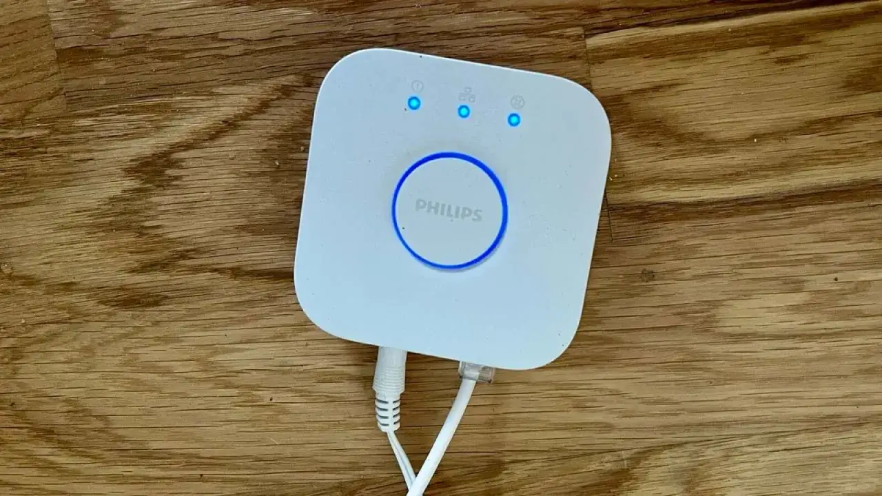 Philips Hue Bridge auf Holztisch. Die blaue Leuchte zeigt die Verbindung an, wichtig für die Hue Bridge Reichweite.