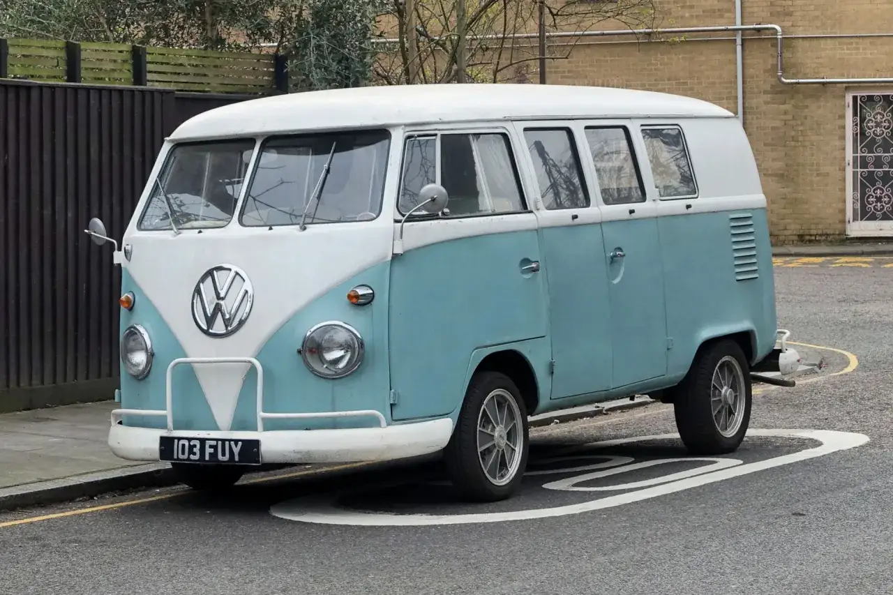Klasyczny VW T1 w kolorze błękitnym i białym, zaparkowany na ulicy.