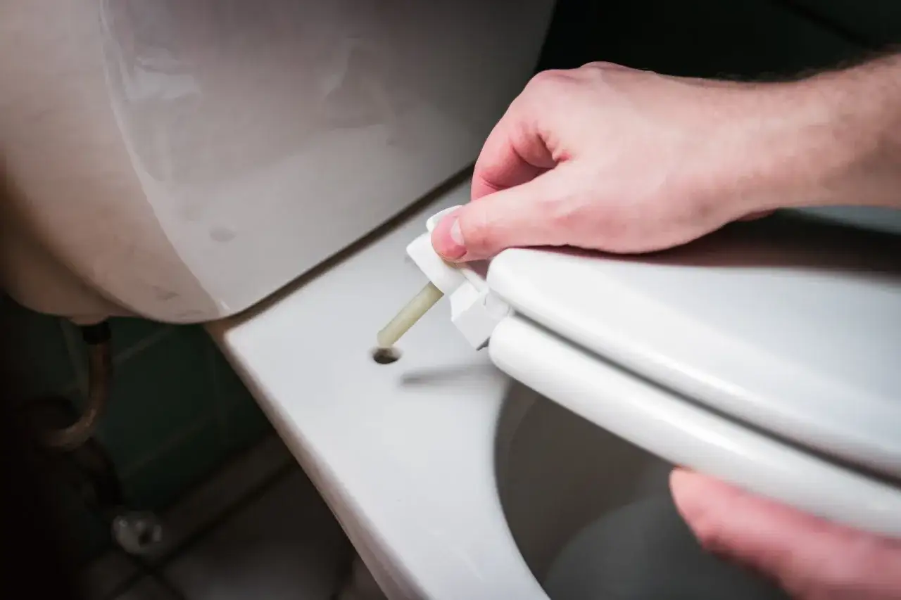 Dłoń przykłada element do sedesu, pokazując, jak zmierzyć deskę sedesową.