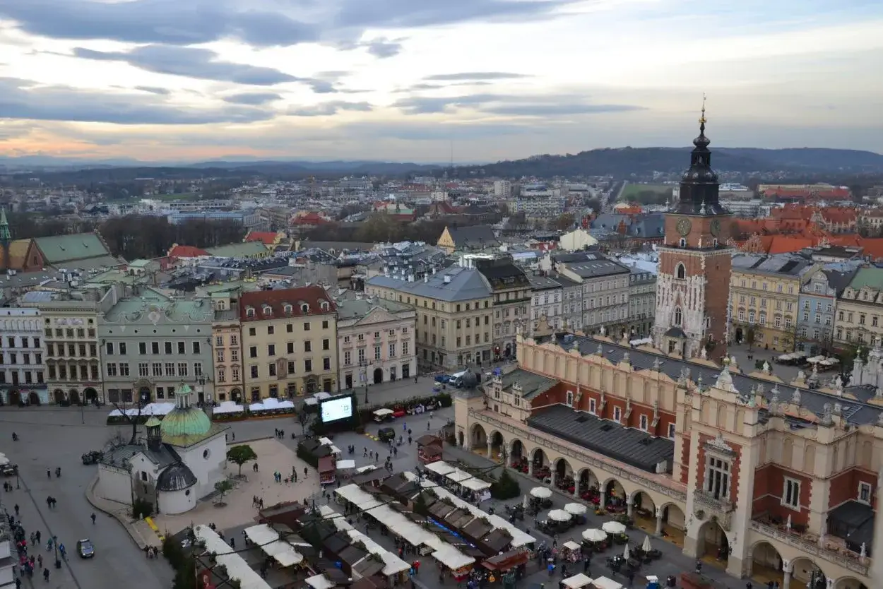 Widok na Rynek Gł&oacute;wny w Krakowie z dominującą wieżą Mariacką. Widać Sukiennice, kolorowe kamienice i targowisko.