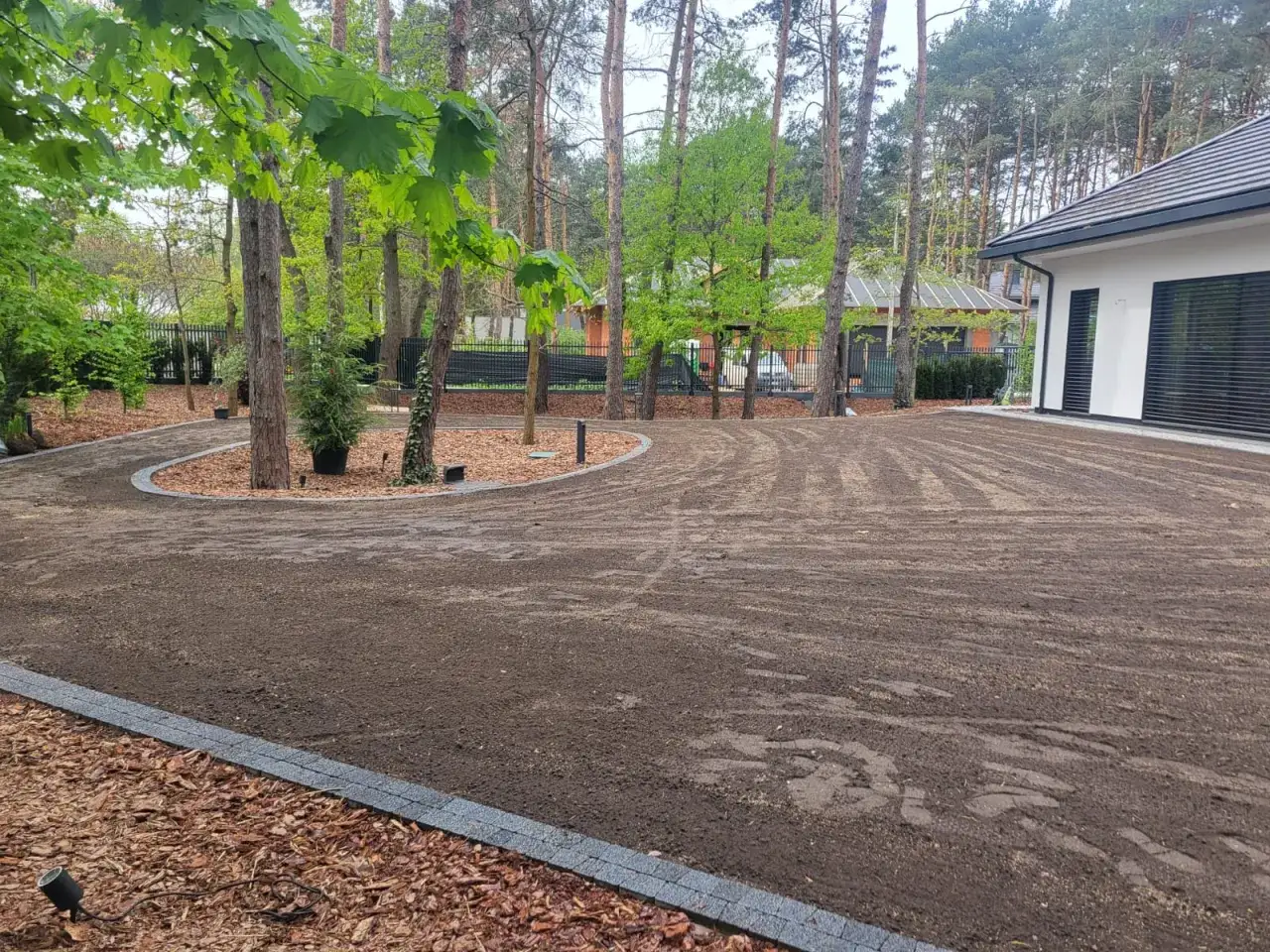 Teren wok&oacute;ł domu przygotowany do założenia trawnika. Widać świeżo przekopaną ziemię, kt&oacute;ra czeka na wyr&oacute;wnanie.