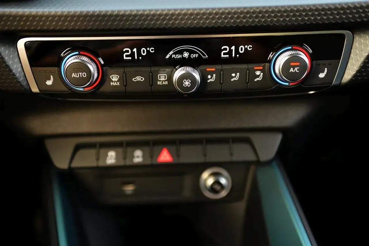 Panel klimatyzacji w aucie z cyfrowym wyświetlaczem 21°C. Widoczny przycisk obiegu zamkniętego w aucie.