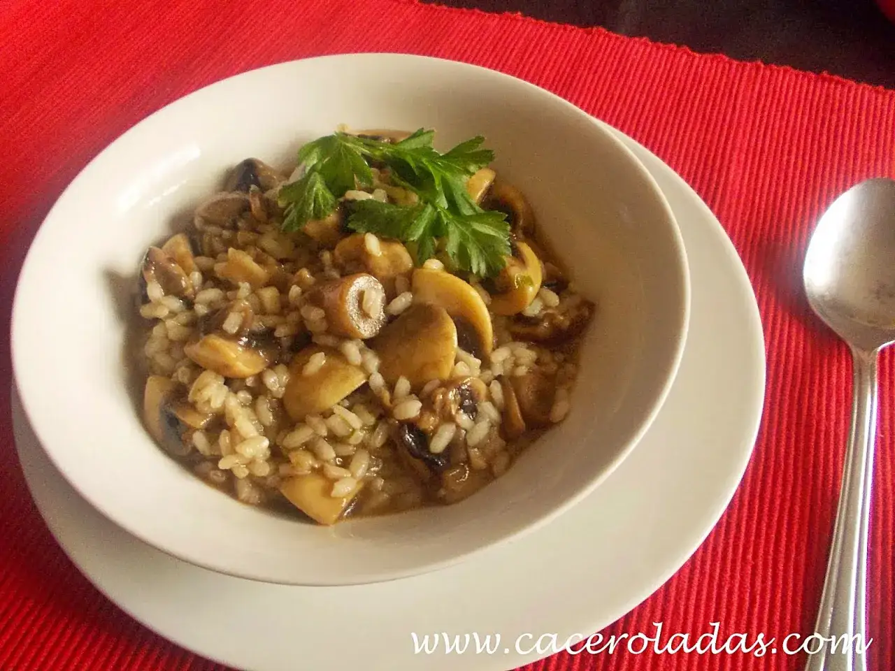 Un delicioso arroz con champiñones, cremoso y aromático, servido en un cuenco blanco y adornado con perejil fresco.