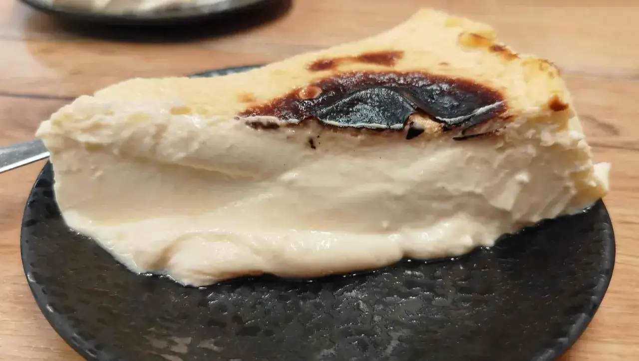 Porci&oacute;n cremosa de pastel vasco, con su caracter&iacute;stica capa superior tostada, servida en plato negro.