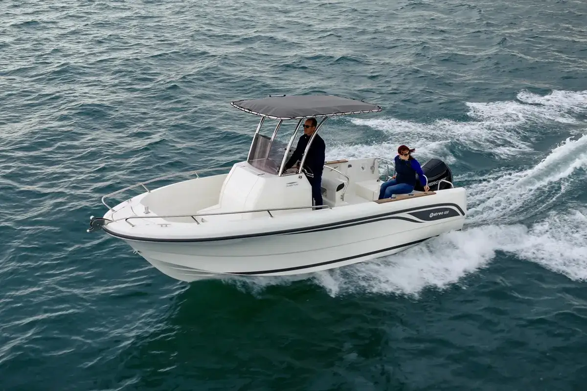 Un bateau blanc, un Ostrea 600, navigue sur une mer agitée. Deux personnes profitent de la balade.