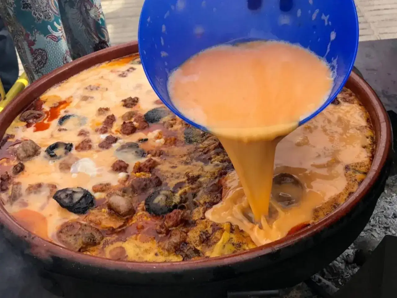 Se vierte un líquido anaranjado sobre un guiso con carne y marisco, un plato de comida típica de Elche.
