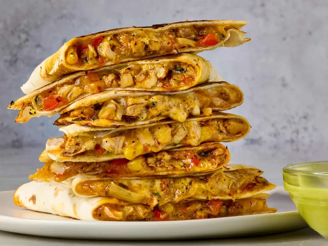 Stos pysznych quesadilli z kurczakiem, serem i warzywami, podanych z zielonym sosem.