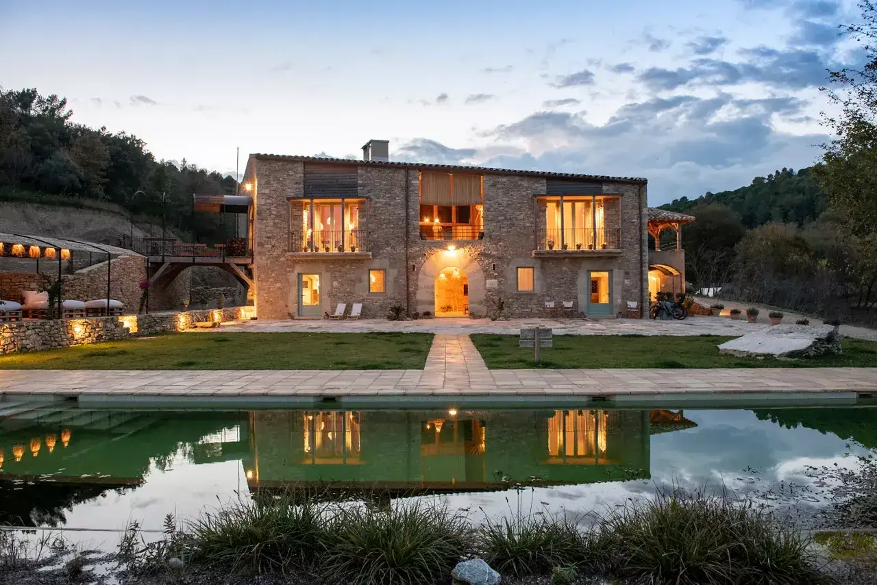 El restaurante El Castell de Brunyola, una mas&iacute;a de piedra iluminada al atardecer, con piscina reflejando sus luces y rodeada de naturaleza.