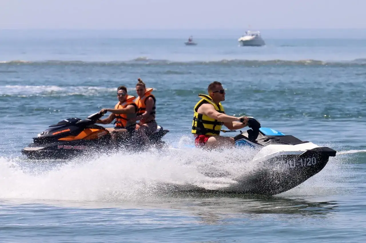 Tres personas disfrutan de los planes en la playa, surfeando en motos acuáticas y creando un gran spray de agua.