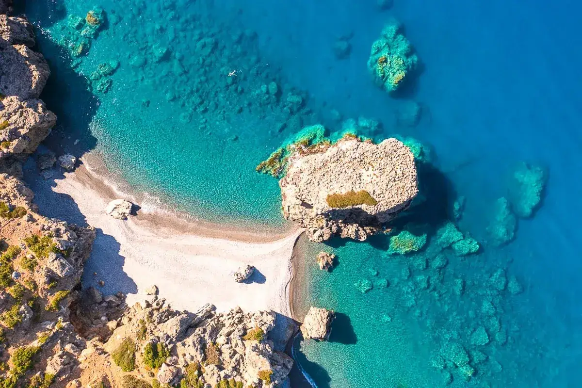 Traumhafte Bucht bei Paleochora, Kreta. Türkisblaues Wasser umspült eine kleine Kiesbucht, Felsen ragen aus dem Meer.