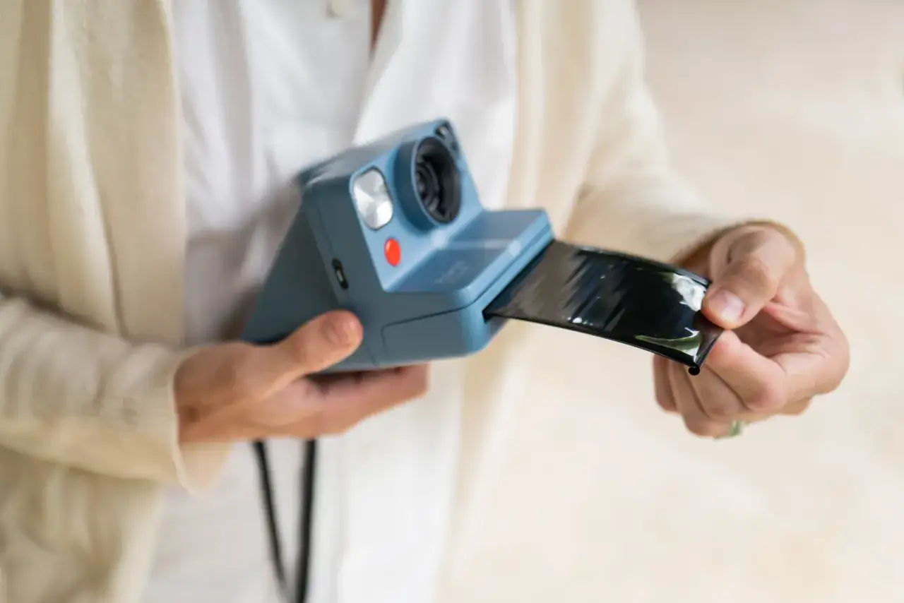 Niebieski aparat Polaroid właśnie wypuszcza błyszczący, czarny film. To jest właśnie to, co to jest!