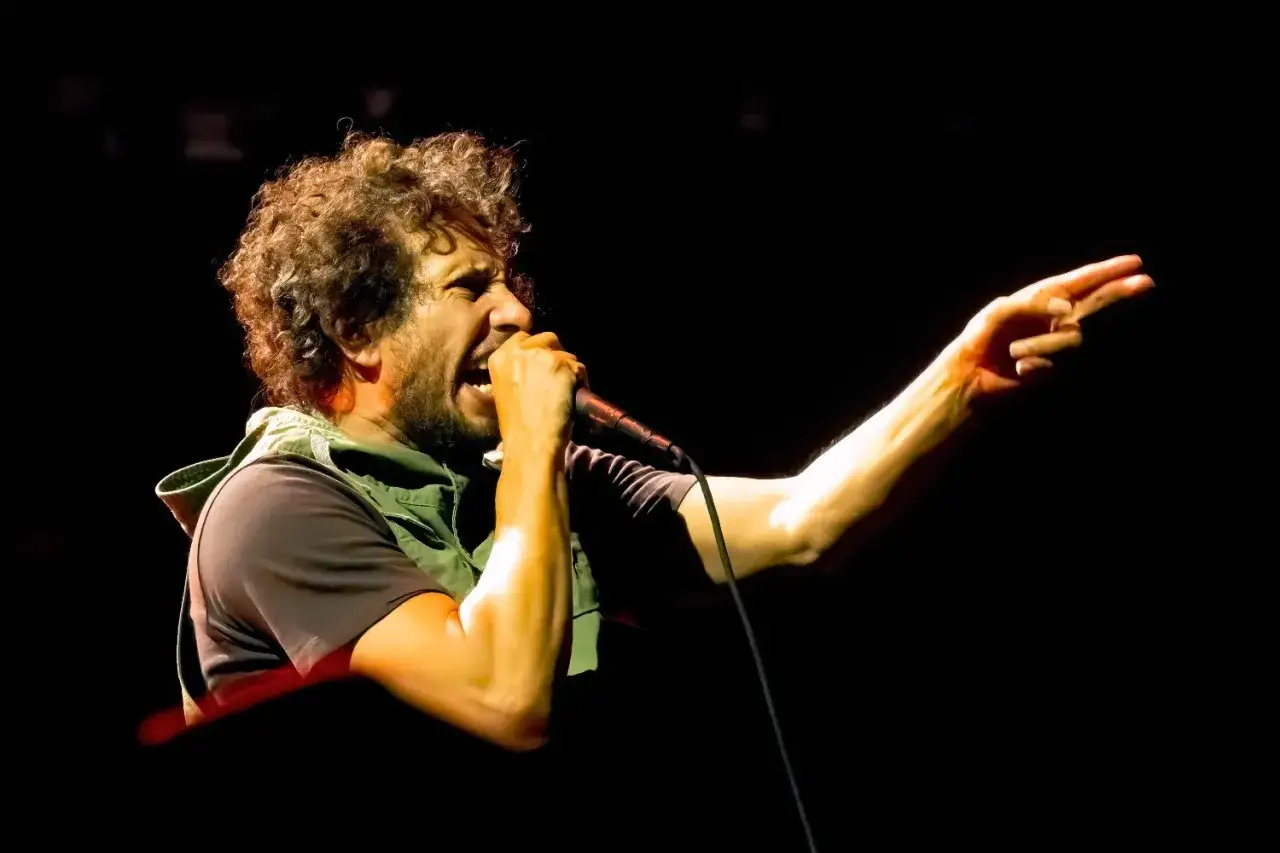 Zack de la Rocha heute: energiegeladen mit Mikrofon und ausgestrecktem Finger, seine Stimme hallt durch die Dunkelheit.