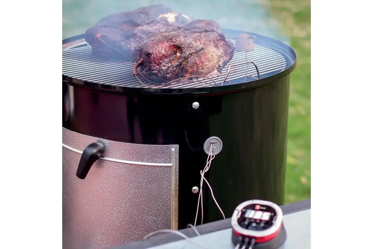 Två stora köttbitar ryker på en grill, redo för amerikansk barbeque. En digital termometer visar temperaturen.
