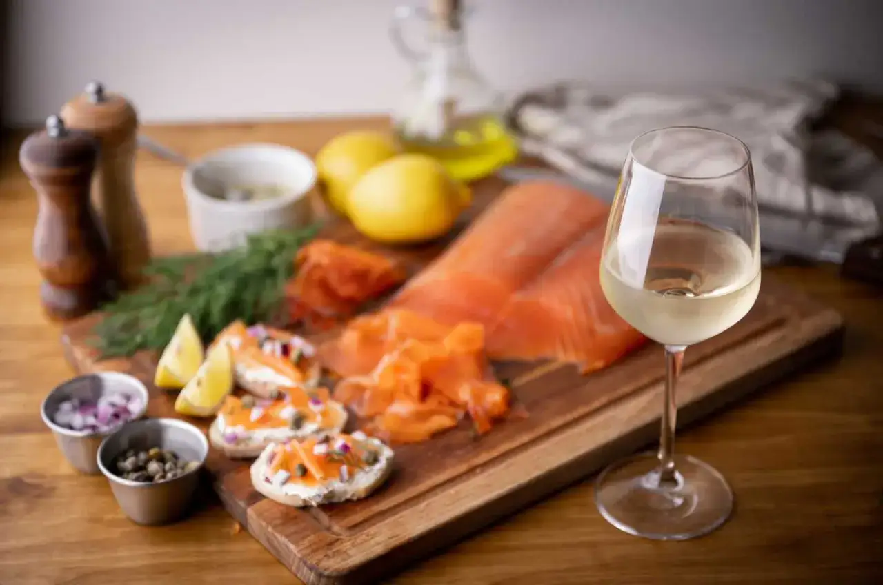 Ein Glas Wei&szlig;wein neben Lachs, Zitronen und kleinen Broten mit Lachs. Die perfekte Antwort auf die Frage: welcher Wein zu Lachs.