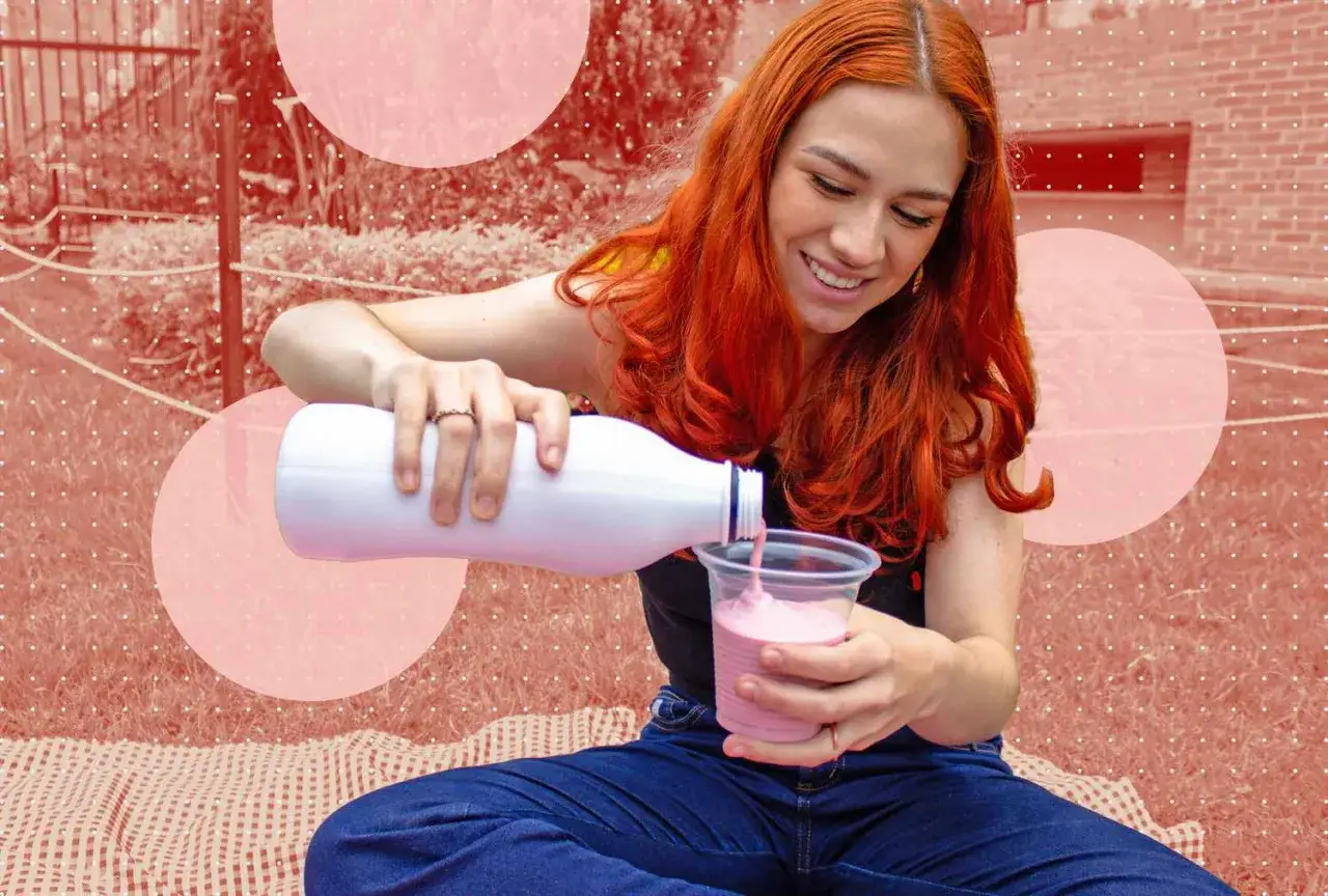 Ragazza con capelli rossi versa kefir rosa in un bicchiere, godendosi un momento di relax serale.