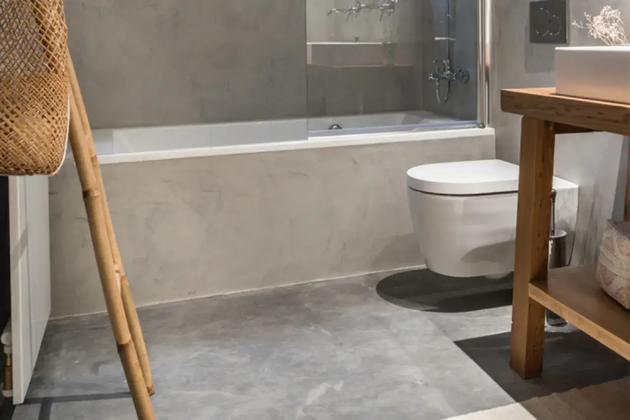Ba&ntilde;o moderno con paredes y suelo de micro mortero. Se ve una ba&ntilde;era, un inodoro suspendido y un mueble de madera.