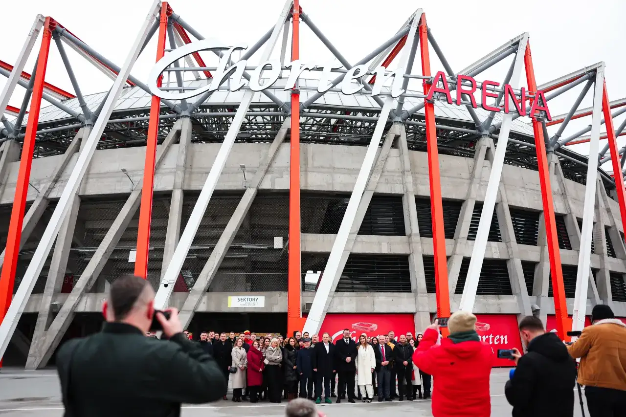 Grupa ludzi pozuje przed stadionem z napisem