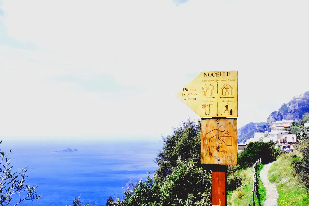 Signpost for il chiosco del sentiero degli dei, pointing to Nocelle, Piazza Santa Croce, and Belvedere. The sea stretches out beyond.