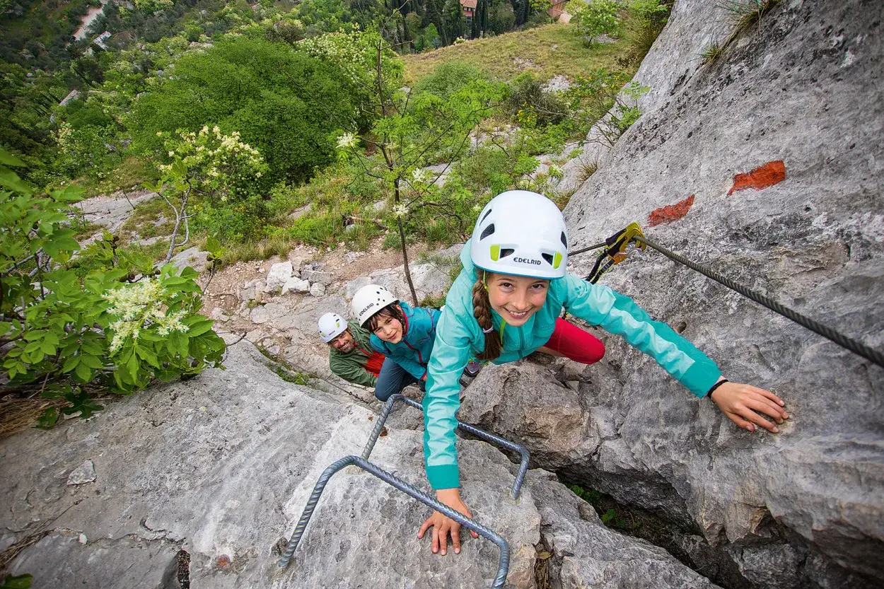 Gl&uuml;ckliche Kinder und ein Mann klettern einen Klettersteig mit Stahlseilen und Trittb&uuml;geln. Ein spannendes Abenteuer f&uuml;r die ganze Familie.