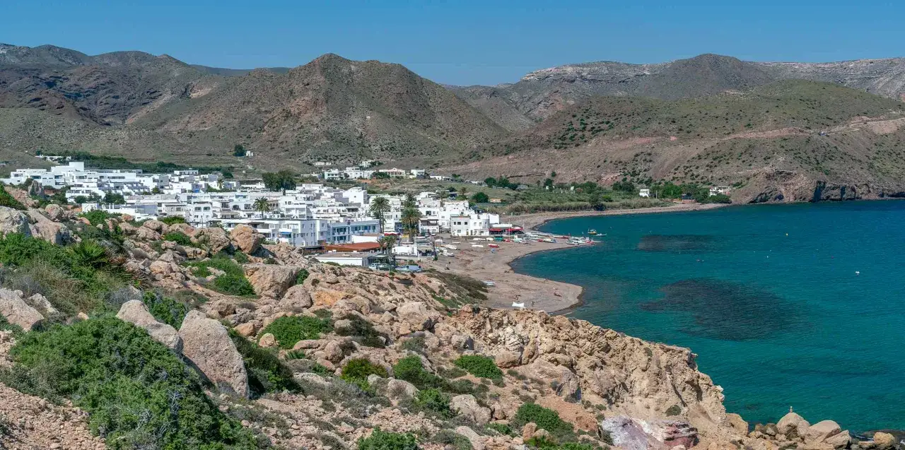 Vista de un pueblo blanco junto al mar turquesa, con montañas áridas al fondo. Un lugar perfecto para un socorrito las negras.