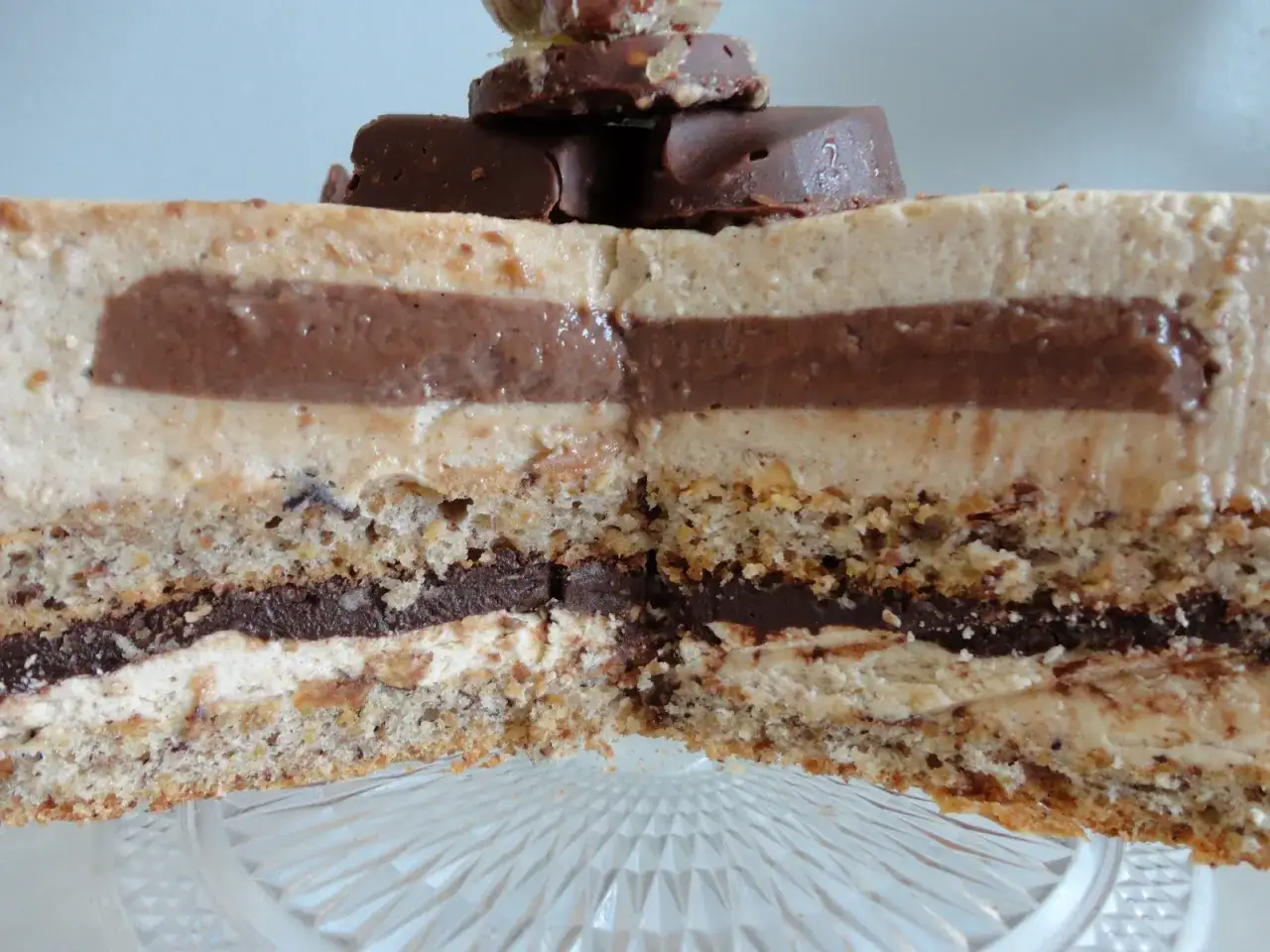 Tranche d'un gâteau aux couches de mousse légère et de ganache chocolat, sur une base de dacquoise noisette croustillante. Décoré de morceaux de chocolat.