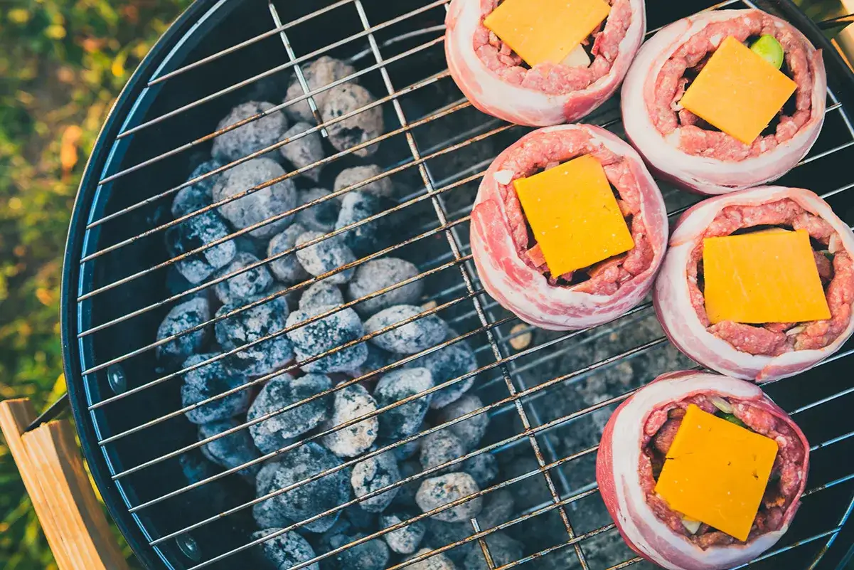 Fem baconsnurrade k&ouml;ttf&auml;rsbiffar med ost p&aring; en grill f&ouml;r indirekt grillning.