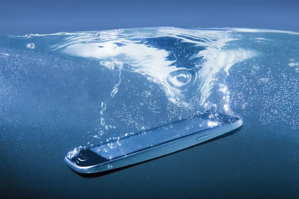 Smartfon z certyfikatem **IP67** zanurza się w wodzie, tworząc wir i bąbelki.