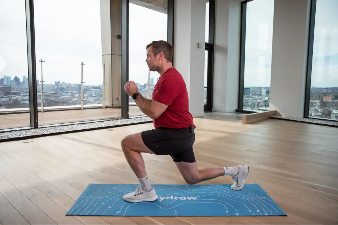 Un homme en tenue de sport fait un fente sur un tapis bleu, un exercice efficace pour comment muscler ses cuisses. La vue sur la ville est impressionnante.