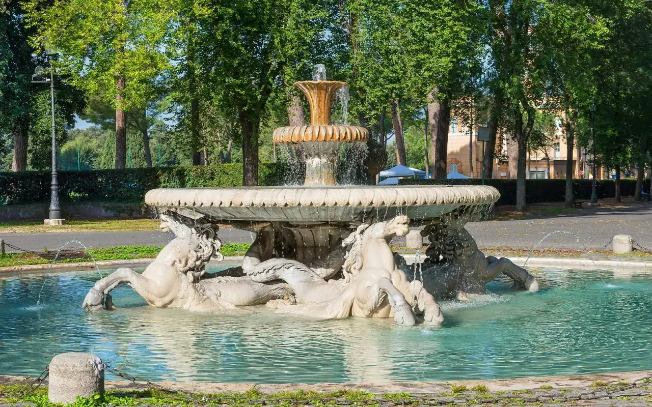 Fontaine de la Villa Borghese avec des chevaux de marbre dans l'eau, sous des arbres verdoyants.
