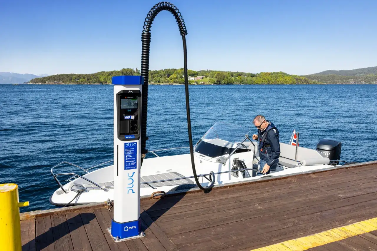 Un uomo collega un cavo a un piccolo yacht elettrico ormeggiato a un pontile, vicino a una colonnina di ricarica.