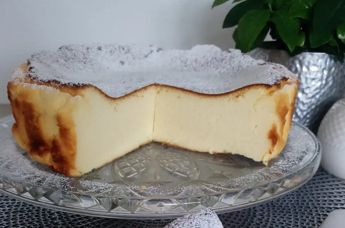 Puszysty sernik z mlekiem skondensowanym, posypany cukrem pudrem, prezentuje się apetycznie na szklanej paterze.