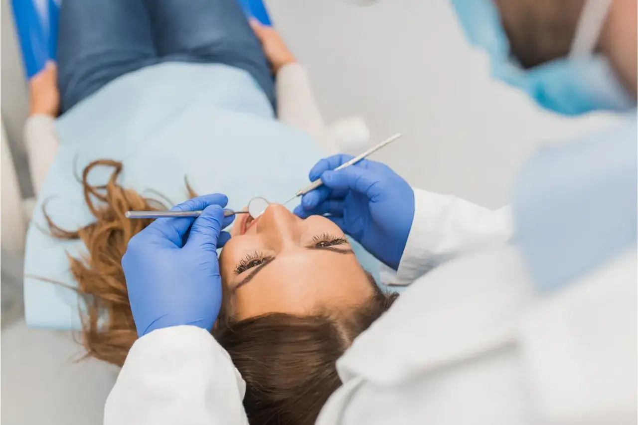 Dentysta w niebieskich rękawiczkach wykonuje zabieg **stripping zębów** u pacjentki leżącej na fotelu.