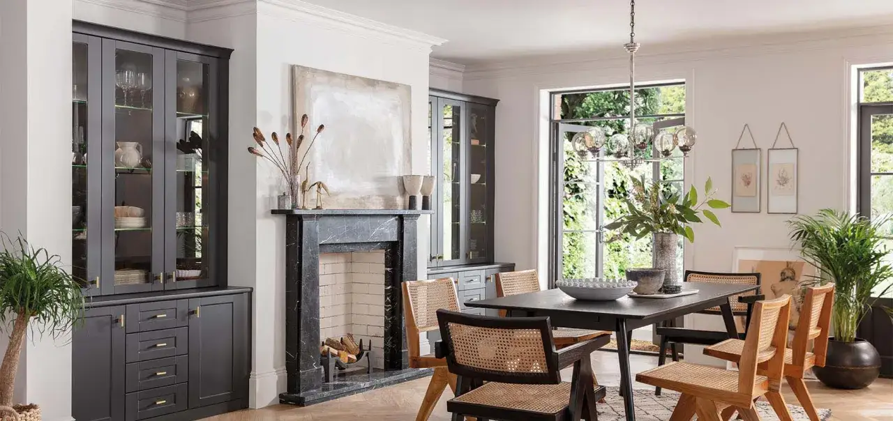 Modern dining room featuring dark grey cabinets, a marble fireplace, and a dark wood table with cane-backed chairs, showcasing current trends in dining room furniture.