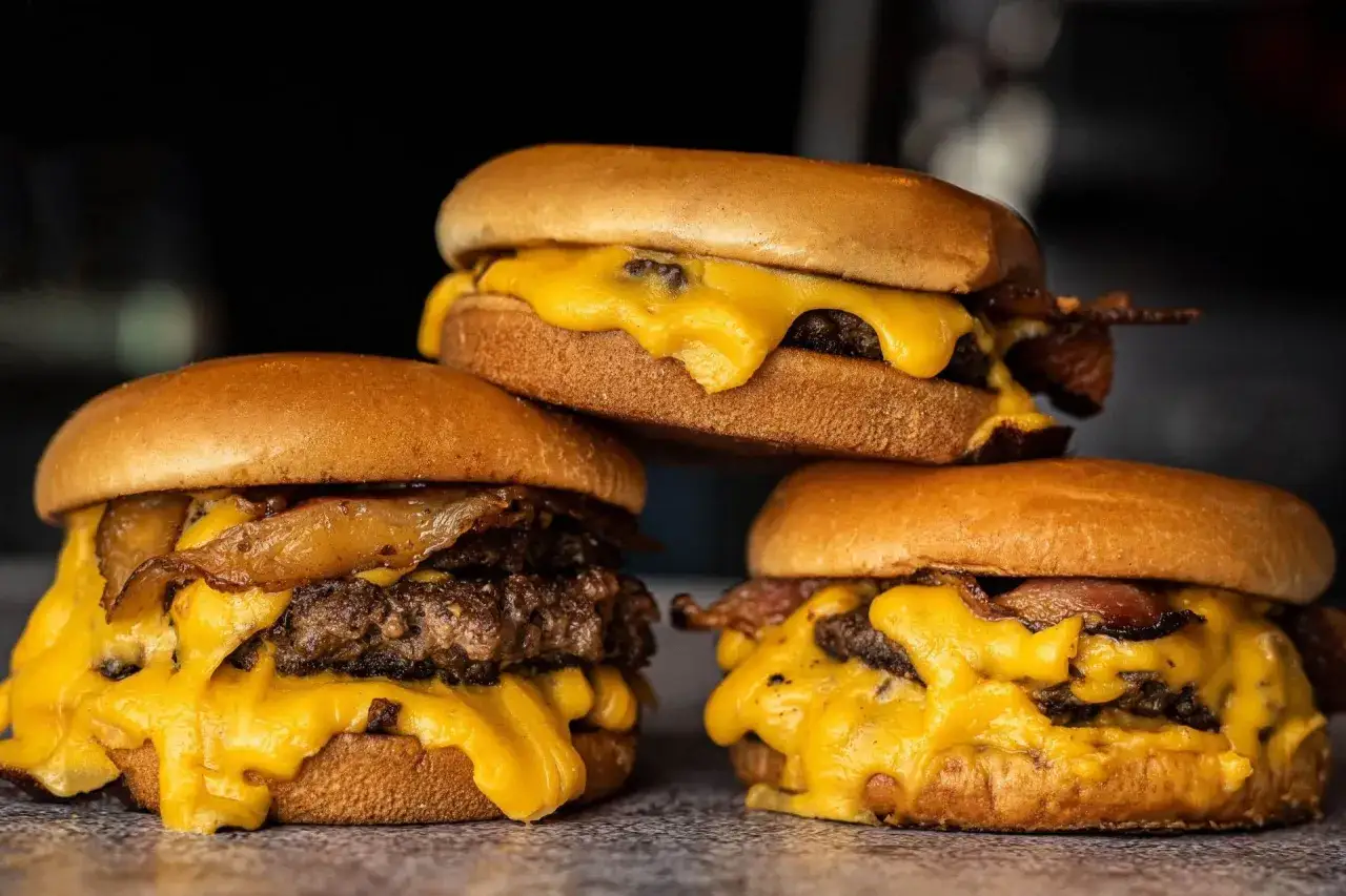 Drei saftige Burger mit geschmolzenem K&auml;se und knusprigem Speck, bereit zum Burger grillen.