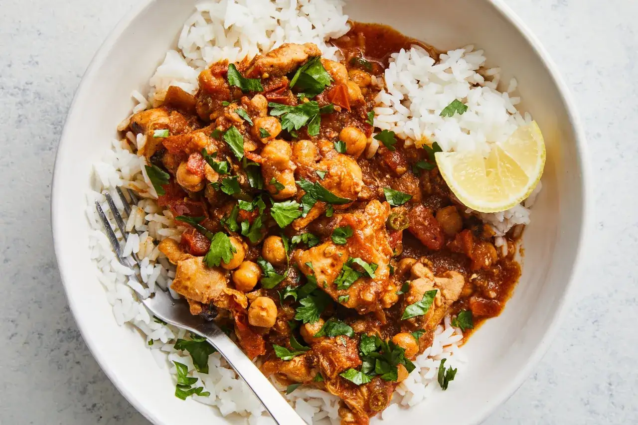 Un plato de arroz al curry con pollo, garbanzos y perejil fresco, adornado con una rodaja de lim&oacute;n.