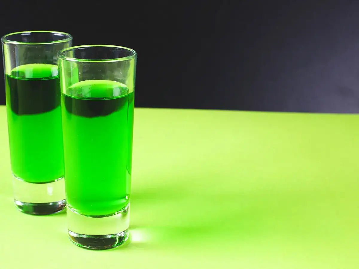 Deux verres de liqueur verte, évoquant une recette chartreuse, sur fond contrasté.